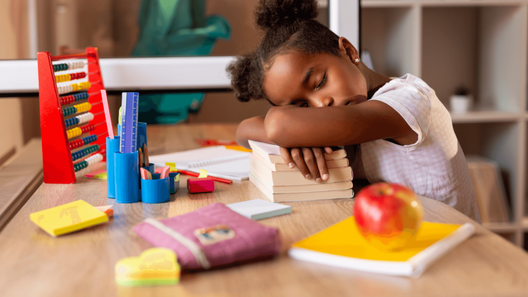 Young girl sleeping at a desk with her head on stacked books, surrounded by school supplies, an abacus, and a red apple.